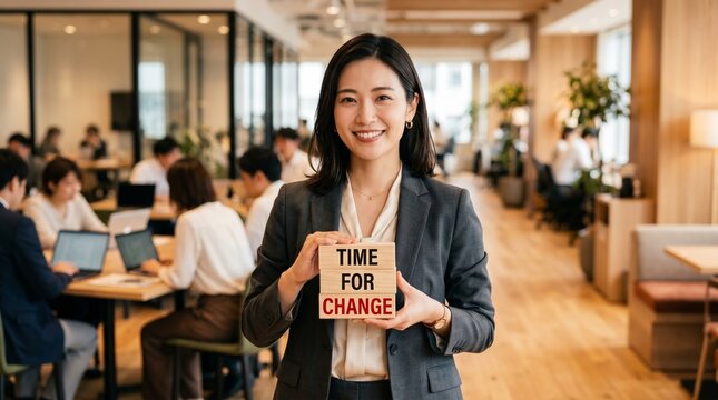 Woman holds a sign reading time for change in a modern office lobby, while coworkers work in the background, illustrating transformation, motivation, and business transition.