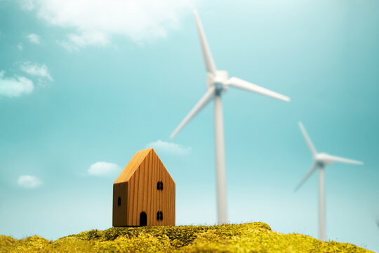Small wooden house with wind turbines under blue sky representing renewable energy, sustainable living and green environment concepts