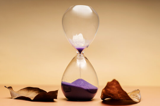 Hourglass with dried leaves, aging process, seasonal life transition and passing lifetime