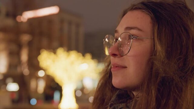 Caucasian woman profile with glasses under golden tree bokeh, warm city night, closeup expression of quiet wonder, rosy cheeks, flowing hair, urban skyline and lamppost lights blurred, artistic mood,