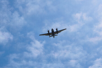 Twin engine propeller aircraft viewed from below as it flies through textured clouds in a blue sky. © PJSCreativeWorks