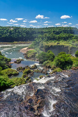 Fototapeta premium Panoramic view of the majestic Iguazu Falls in Iguazu National Park, surrounded by lush tropical rainforest under a clear blue sky with white clouds