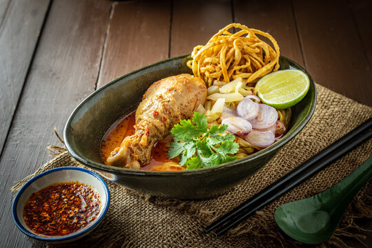 Traditional Khao Soi Kai, a Northern Thai chicken egg noodle curry with crispy noodles, lime, and red onions in a dark bowl, captured in a rustic food photography style for Asian cuisine design.