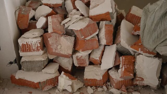 Closeup view of broken red bricks and white plaster rubble piled up during demolition or renovation work showing rough texture and debris