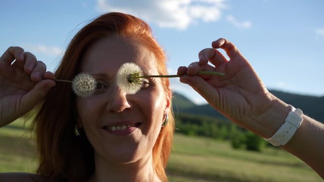 Beautiful redhead woman having fun in nature on a warm summer evening. Green mountains and the blue sky in the background. Summer holidays and outdoor recreation concept
