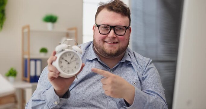 Overweight man accountant businessman in office. Smiling worker points at clock, notes deadline and schedule. Pile of paperwork shows workload, productivity. Solid clear time management concept.