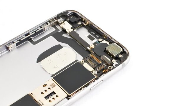 Open smartphone under maintenance on a white surface, revealing its internal complexity. Close view of a disassembled phone for maintenance on a white base, exposing its inner structure.