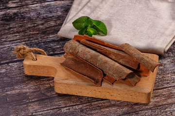 Aromatic cinnamon bark pieces with fresh mint leaf on rustic cutting board © Andrei Starostin