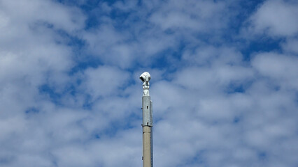 Obraz premium White security cctv camera mounted on a tall pole against a blue sky with white clouds