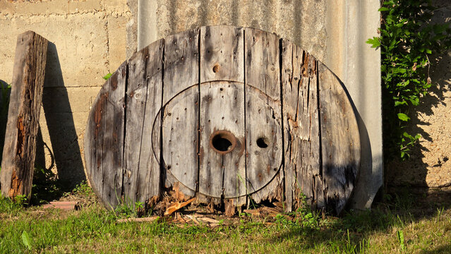Weathered wooden cable spool flange with concentric rings and center hole leaning against concrete wall
