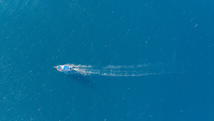 Fototapeta premium A minimalist drone shot of a single boat gliding across the deep blue, endless sea, leaving a trail of white foam in its wake.