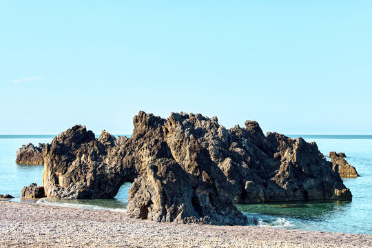 Scenic view of Ajiella beach with volcanic rocks and natural arch in Scalea, Calabria, Italy. Beautiful Mediterranean sea coast on a sunny day.