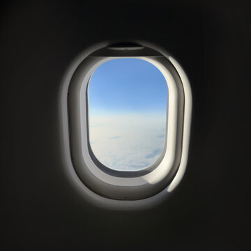 View of blue sky and clouds through airplane window from inside cabin