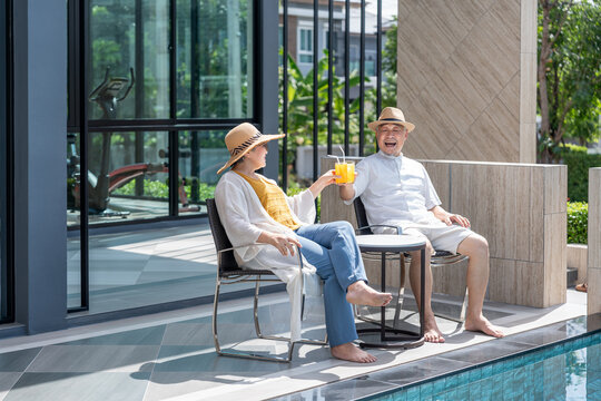 happy senior couple enjoy talking with freshy drink on table,sitting,relaxing by the pool,elderly people travel destination tropical resort and spa on summertime