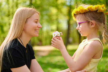 Fototapeta premium A cute little girl gives flowers to her mother in the park. Mother's day concept. Happy family.
