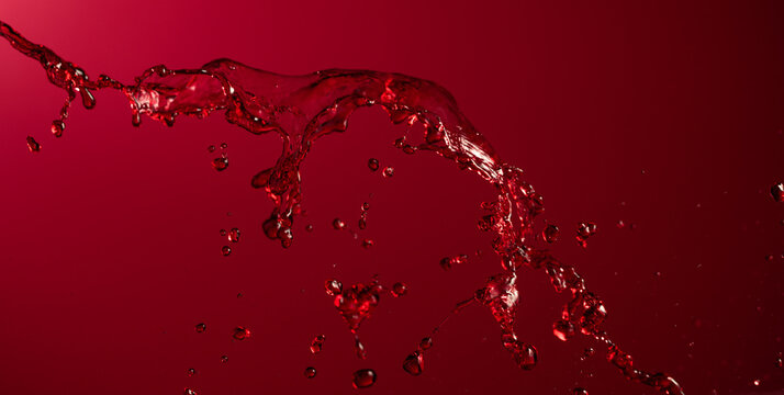 Glass and red wine splash on a dark red background.