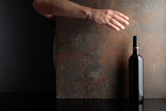 Hand reaches for a bottle of red wine.