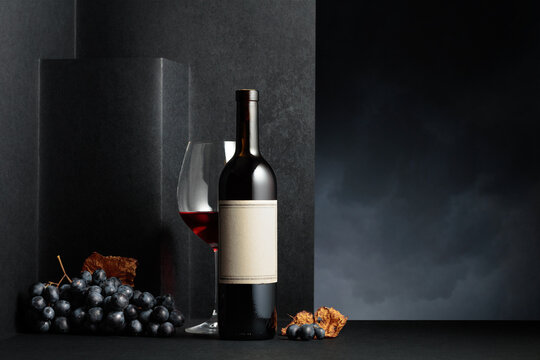 Red wine and blue grapes with dried up vine leaves on a black background.