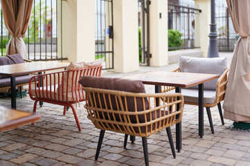 Fototapeta premium Outdoor cafe with wicker chairs and tables on a stone floor. Cozy terrace for relaxing and eating.