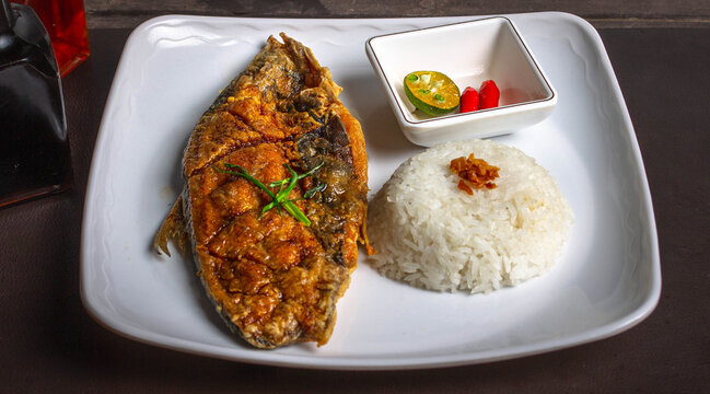 close up photo of deep fried bangus also known as milk fish with garlic fried rice, red chili pepper and lemon for sauce on a white square plate.
