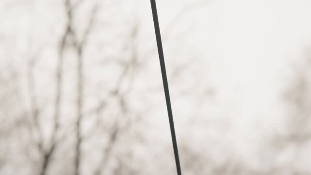 Closeup of metal swing hardware and hanging cable, midair childs feet above cracked rubber surface, focus on texture and tension, muted overcast sky and bare branches in background, intimate technical