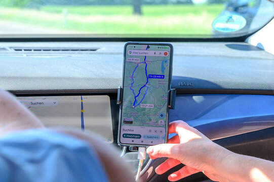 Augsburg, Germany &mdash; May 31 2026: A passenger adjusts a smartphone mounted on the car dashboard showing a Google Maps route overview with Buchloe as a destination