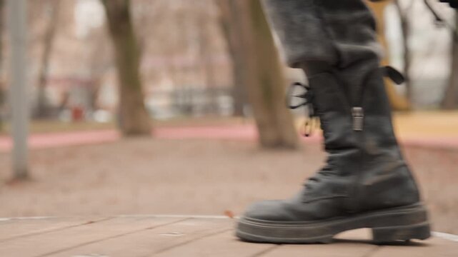 Caucasian woman boots stepping on platforms closeup, black leather boots landing on circular spring discs, emphasis on sole grip and laces, muted autumn park background, rhythmic heavy steps