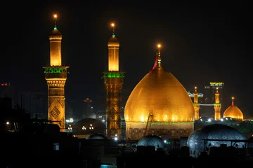 Fototapeten Schwarz Karbala, Iraq - December 28, 2025: Golden dome and illuminated minarets of the Imam Hussain Shrine glowing at dusk in Karbala, Iraq  © hasan