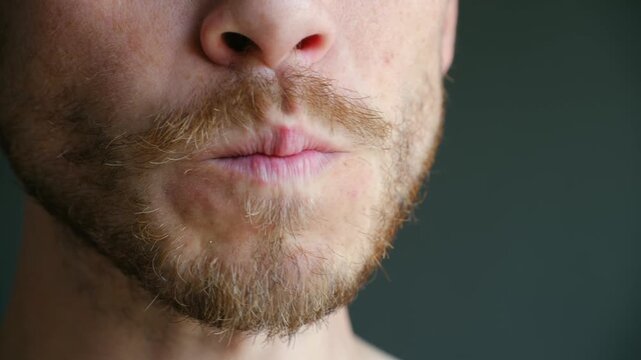 Close up man with beard putting potato chip in mouth, chewing with satisfaction, showing pleasure of eating tasty but unhealthy snack on dark background. Bearded man mouth close up eating potato chips