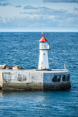 Obraz premium Lighthouse of norwegian town Vardo with blue sea and clouds in the background