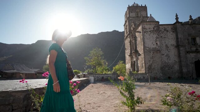 Mature woman enjoys a sunrise adventure in the garden by San Javier Mission, smiling and experiencing the beauty of Baja California Sur