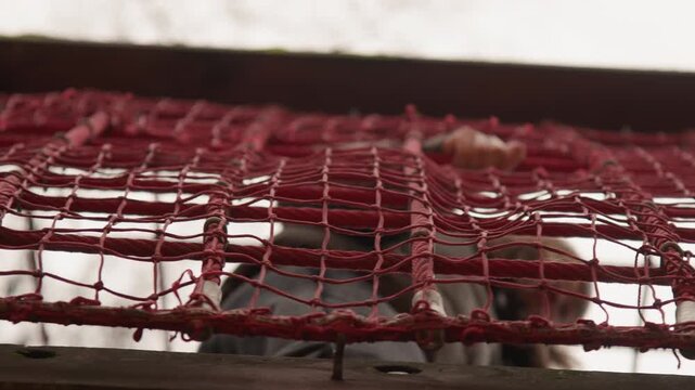 Worn red net on frame, closeup study of frayed fibers and grid pattern, backlit by soft window light, weathered wooden sill and rusted metal fasteners, tactile texture and urban decay mood, versatile