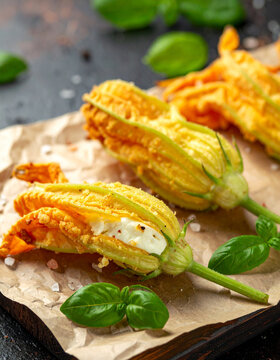 Delicate zucchini blossoms stuffed with ricotta cheese and deep fried until golden on a rustic paper-lined wooden board.