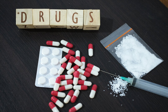 DRUGS, A syringe with pills, medication tablets, and a package of methamphetamine or heroin on a wooden table. The concept of drug trafficking and addiction.