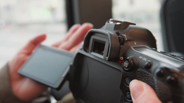 Closeup hands adjusting camera screen, camera technician reviewing settings on flip LCD inside bus, tactile button presses, menu navigation, previewing images and polishing body with cloth.