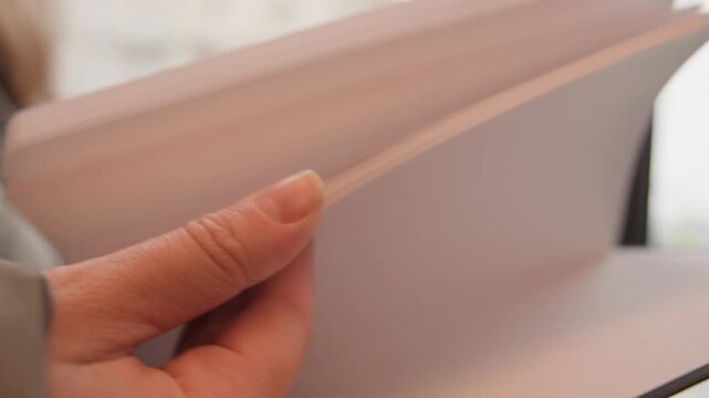 Closeup hands flipping blank pages in notebook, soft window light and blurred city background, cozy cafe vibe person previews sketch mockup, student reviews notes, writer plans layout beige cover