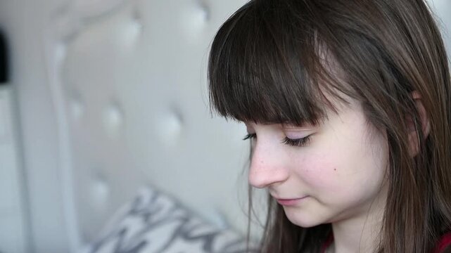 A teenage girl sits in bed and sneezes into a tissue. Colds, seasonal allergies.