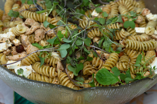 Close-up of a chicken pasta salad with fusilli, feta cheese and fresh microgreens. A macro top-down shot of a fresh pesto pasta salad served in a bowl. 