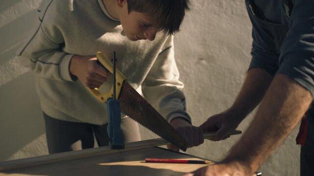 Caring father teaching his son how to safely use a hand saw during a woodworking task, highlighting family bonding, hands on learning, and educational parenting moment.
