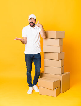 Full-length shot of delivery man among boxes over isolated yellow background making phone gesture and doubting