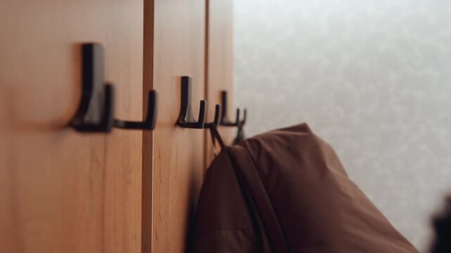 Warm indoor setting with hanging garments. Gentle natural light illuminates cozy home entryway scene. Intimate interior moment showcasing hand hanging coat on rustic wooden hooks in warm ambiance