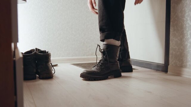 Preparing for outing tying heavy boots, lowangle closeup of black combat boots, socked foot rises, hand reaches to lace, hurried morning or evening routine, wooden floor, textured sole, focused motion