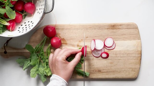 Hands slicing fresh red radishes on a wooden cutting board with a knife. Symbolizes healthy food preparation. Ideal for nutrition, vegan lifestyle, and culinary content. Bright, clean kitchen scene