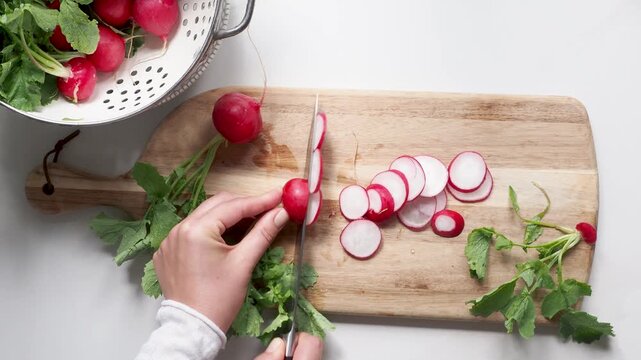 Hands slicing fresh red radishes on a wooden cutting board with a knife. Symbolizes healthy food preparation. Ideal for nutrition, vegan lifestyle, and culinary content. Bright, clean kitchen scene