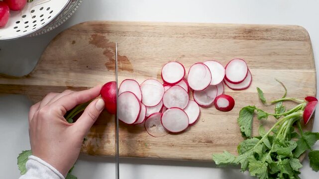 Hands slicing fresh red radishes on a wooden cutting board with a knife. Symbolizes healthy food preparation. Ideal for nutrition, vegan lifestyle, and culinary content. Bright, clean kitchen scene