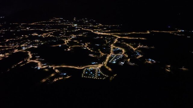 Aerial drone night view of illuminated winding roads and streets in a mountain town, urban nightscape
