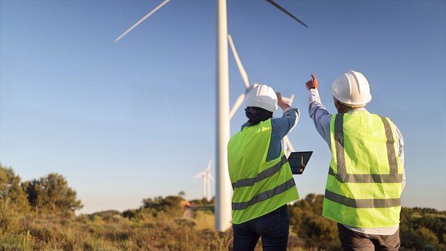 Engineers inspecting wind turbine farm, planning renewable energy solutions for a sustainable future, discussing power generation technology outdoors
