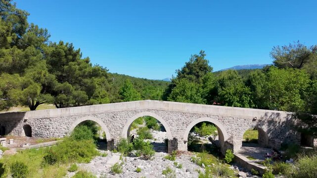 Scenic drone footage captures an ancient stone bridge surrounded by lush green forests and mountains