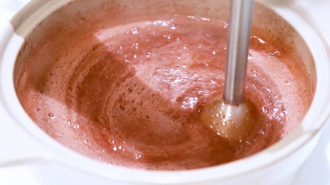 Close up strawberry mixture being blended into a silky smooth consistency during the process of making homemade syrup. The rotating blender creates dynamic swirling patterns and rich pink-red textures
