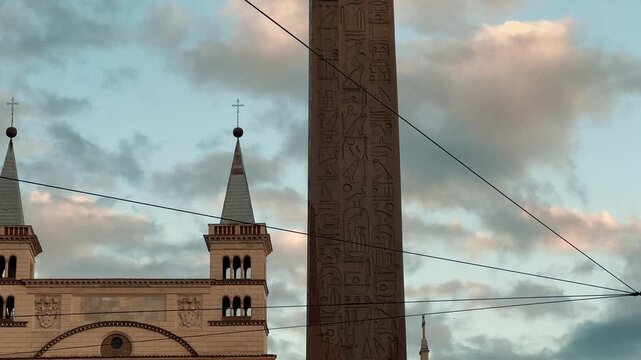 The majestic Lateran Obelisk stands tall in Piazza di San Giovanni in Laterano, Rome, Italy, with traffic passing by under a dramatic, colorful cloudy sky during late afternoon.

